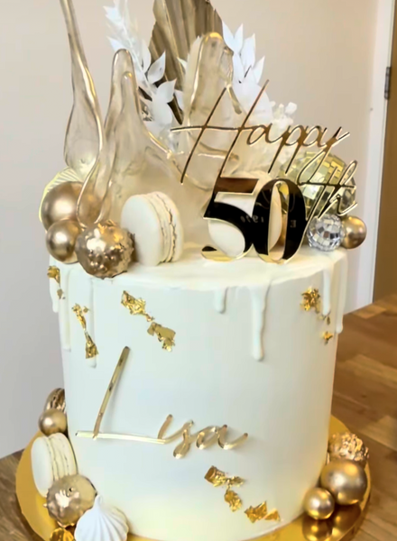 Decorative cake with gold and white elements and 'Happy 50' topper.